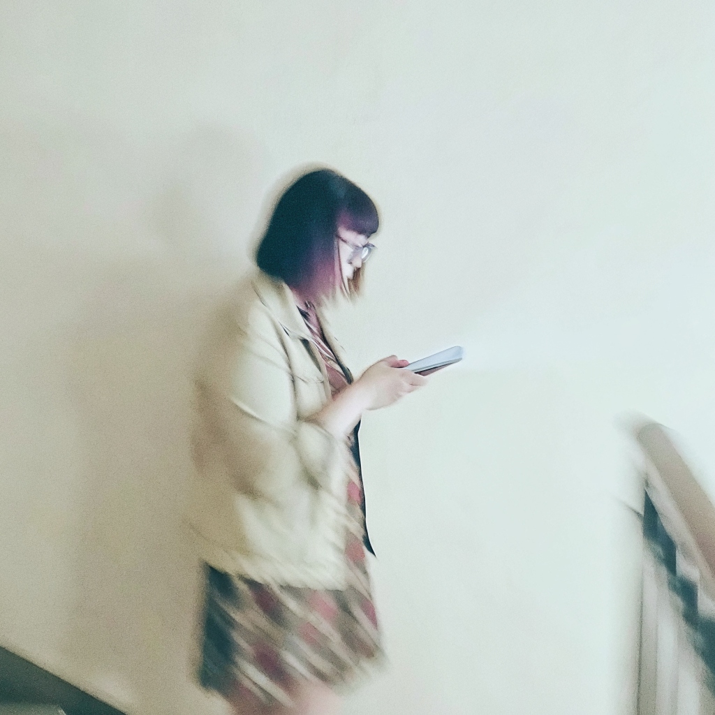 A blurred figure of a woman walking down a stairwell, reading her phone